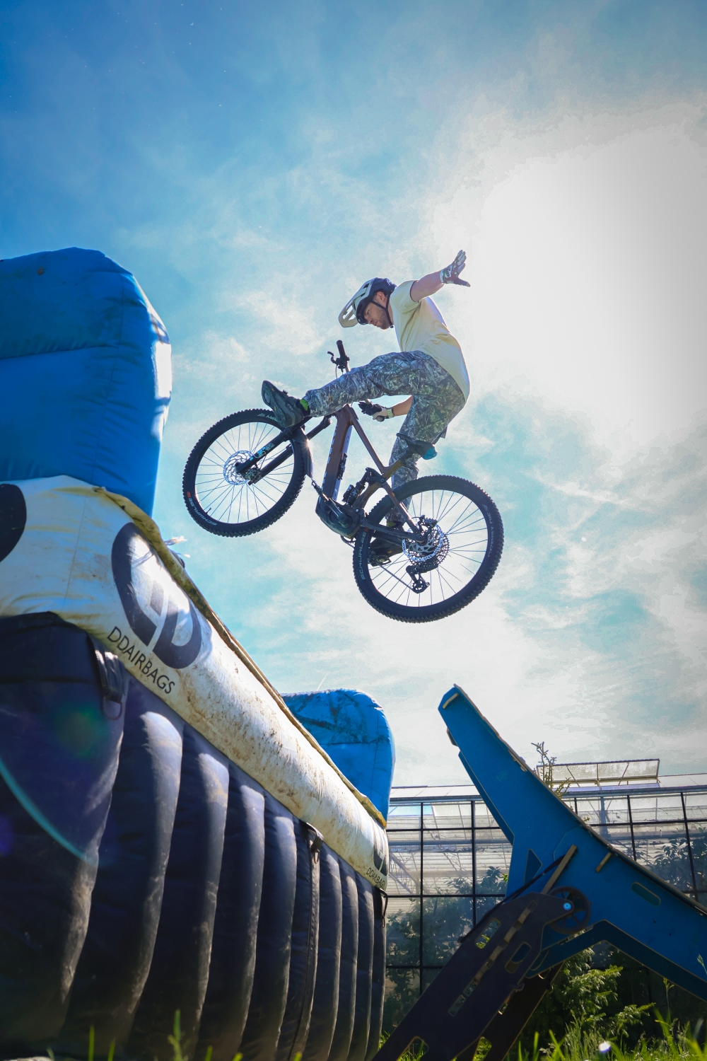 Mountainbiker maakt een sprong over de outdoor airbagjump bij Indoor Mountainbike Almere, met zachte landing op de DDairbags-airbag onder een blauwe zomerhemel