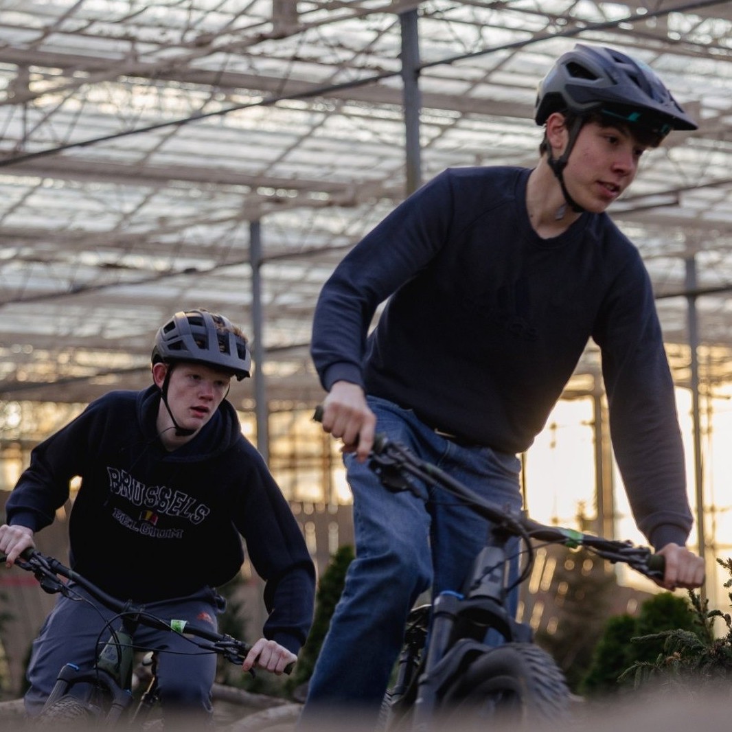 Twee jongeren met helm rijden achter elkaar op mountainbikes over het overdekte parcours van Indoor Mountainbike Almere