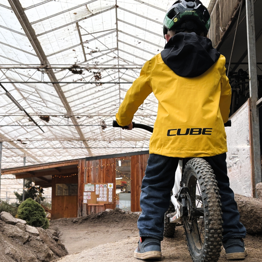 Kind in gele CUBE-jas en helm op een kinderfiets, klaar voor een rondje op het indoor parcours van Indoor Mountainbike in Almere